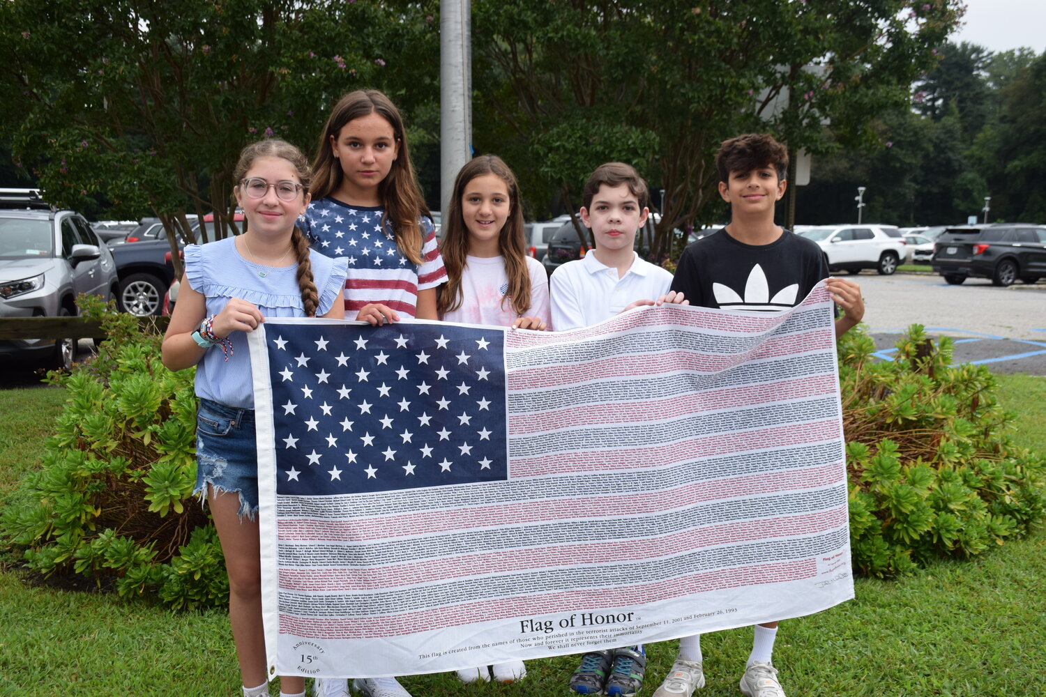 Locust Valley Middle School students Gianna Aldorasi, left, Eva Jaszczuk, Mia Marchand, Christos Pappas and Logan Moran held a flag with the names of all those lives lost during the Sept. 11 attack.