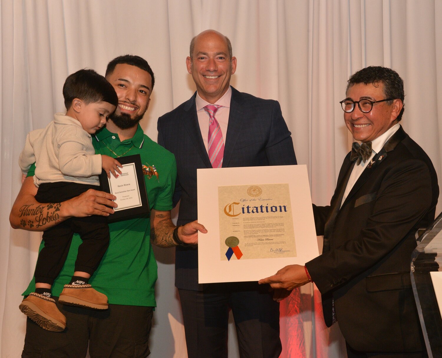 Kevin Rivera, formerly of Uniondale, saved seven members of a family from a house fire in Syosset on Sept. 10, 2022. His 1-year-old son, Kayden, grabbed his father’s Good Samaritan award at the American Red Cross ceremony on Oct. 26, while award presenter Barry Litwin, CEO of Global Industrial, looked on. Jose Dominguez, CEO of the American Red Cross on Long Island, presented Rivera with a citation sent by U.S. Rep. Anthony D’Esposito.