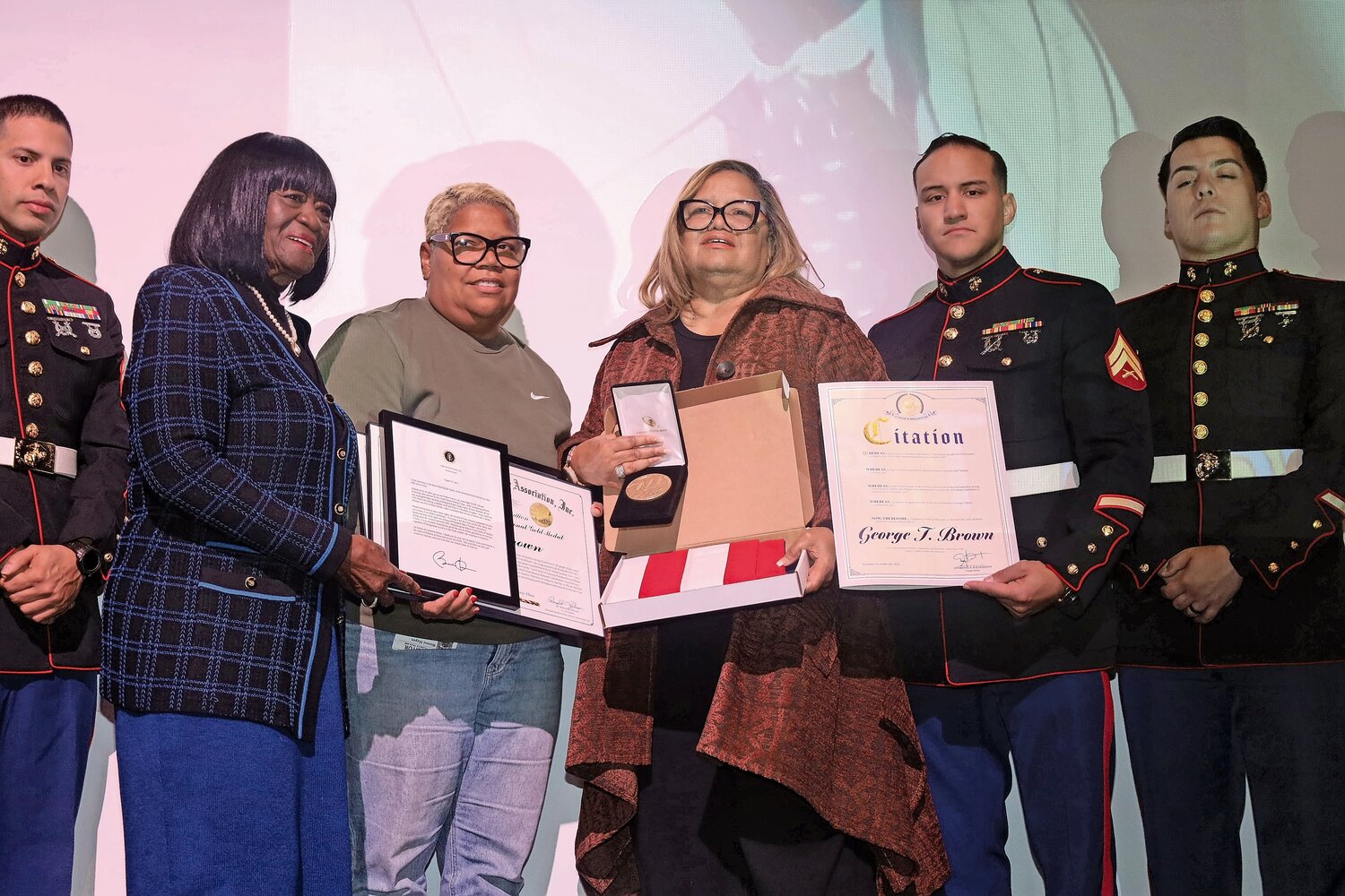 Flanked by active-duty Marines, Olga Brown-Young, fourth from left, and her sister Bimini Brown Hayes, third from left, displayed the honors their father, George T. Brown, received posthumously on Nov. 9 at Hempstead High School: the Congressional Medal of Honor; a framed version of the 2012 statement from President Barack Obama when he awarded the medal to the Montford Point Marines as a group; a U.S. flag sent from Congressman Anthony D’Esposito; and written citations from the National Montford Point Marine Association, Inc., State Senator Kevin Thomas, County Executive Bruce Blakeman, and Deputy Town Executive Dorothy Goosby, who stands second from left in the photo.