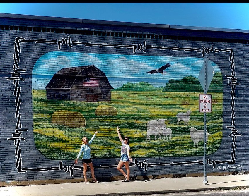(Left to right) Local artist Samantha Cox and Shabby Sheep Boutique owner Lorissa Ellis stand in front of the newest mural in Marshfield: a tribute to farm life, the frontline and Ellis&rsquo; business.