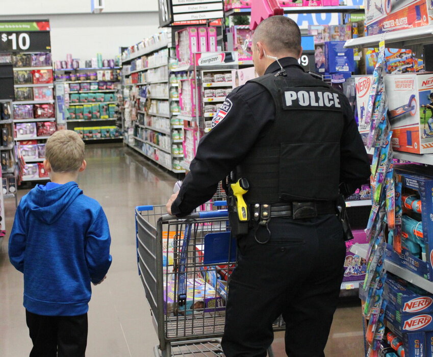 Officer Josh Burris walks the aisle with one of the kids participating in this year's Shop with a Cop. Eagerly, the two look for the best toys to get.   Mail photo by J.T. Jones
