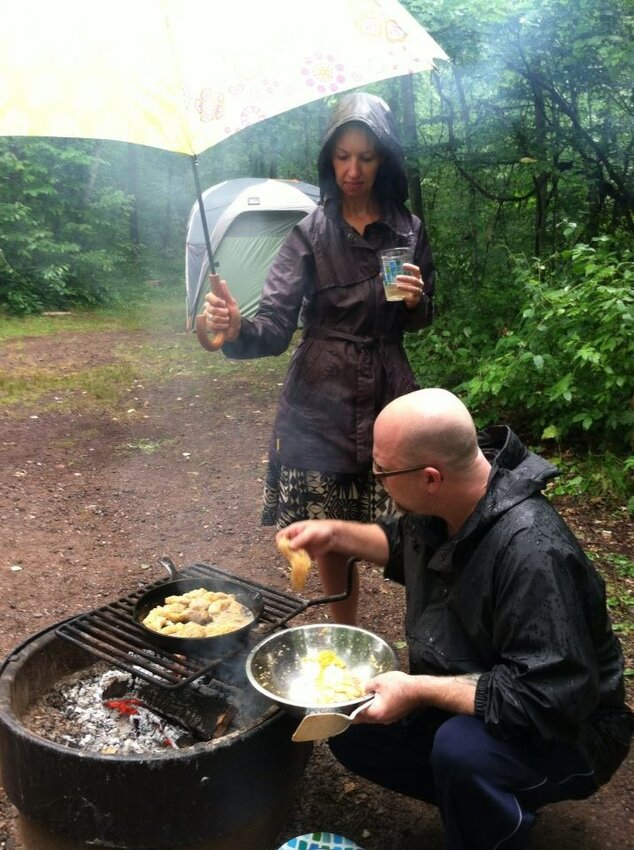 Chef J.D. Fratzke cooks on an open fire while camping as his wife, Lisa Anderson Fratzke, shields the meal with an umbrella. (Photos submitted)