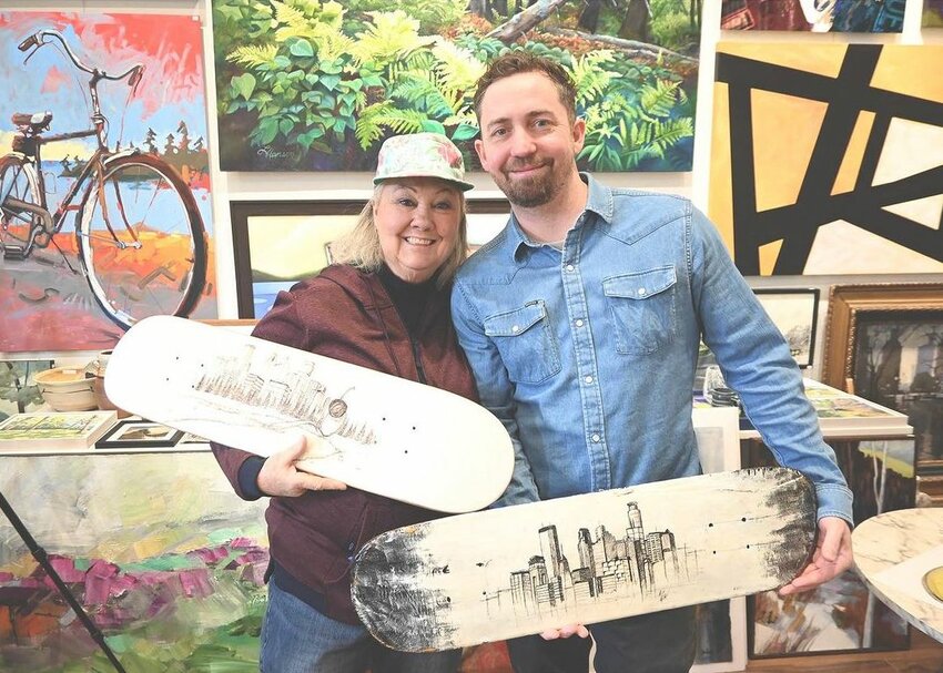 Mark Rivard, at right, holds up the first skateboard art he drew with a sharpie. Next to him, his mom, Lorelli Byrne, holds up an iconic piece he did on another skateboard. (Photo by Tesha M. Christensen)