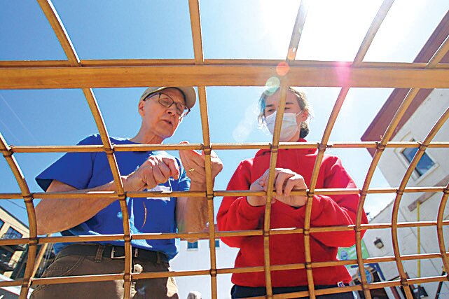 David Walcher of Urban Boatbuilders instructs Masyn May to lace ribs to the frame of a canoe.  Urban Boatbuilders teaches youth how to build boats through paid internships. Gretchen Wilbrandt of Urban Boatbuilders says they seek to let companies know they have employable youth. She cites COVID, global wars, and a mental health crisis as stressors that can make youth feel hopeless.