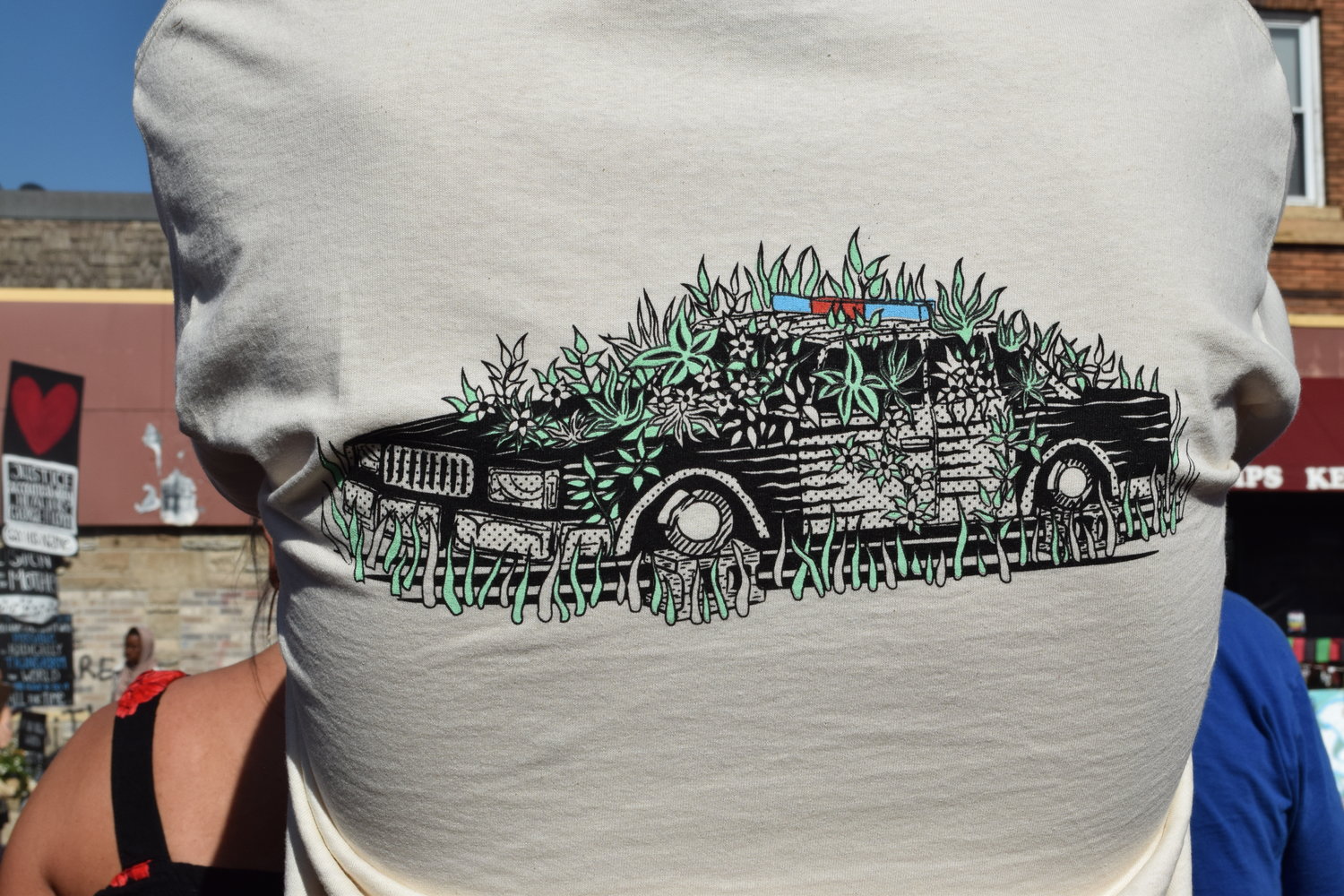 A graphic on the back of someone’s t-shirt shows plants growing out of an idle squad car.