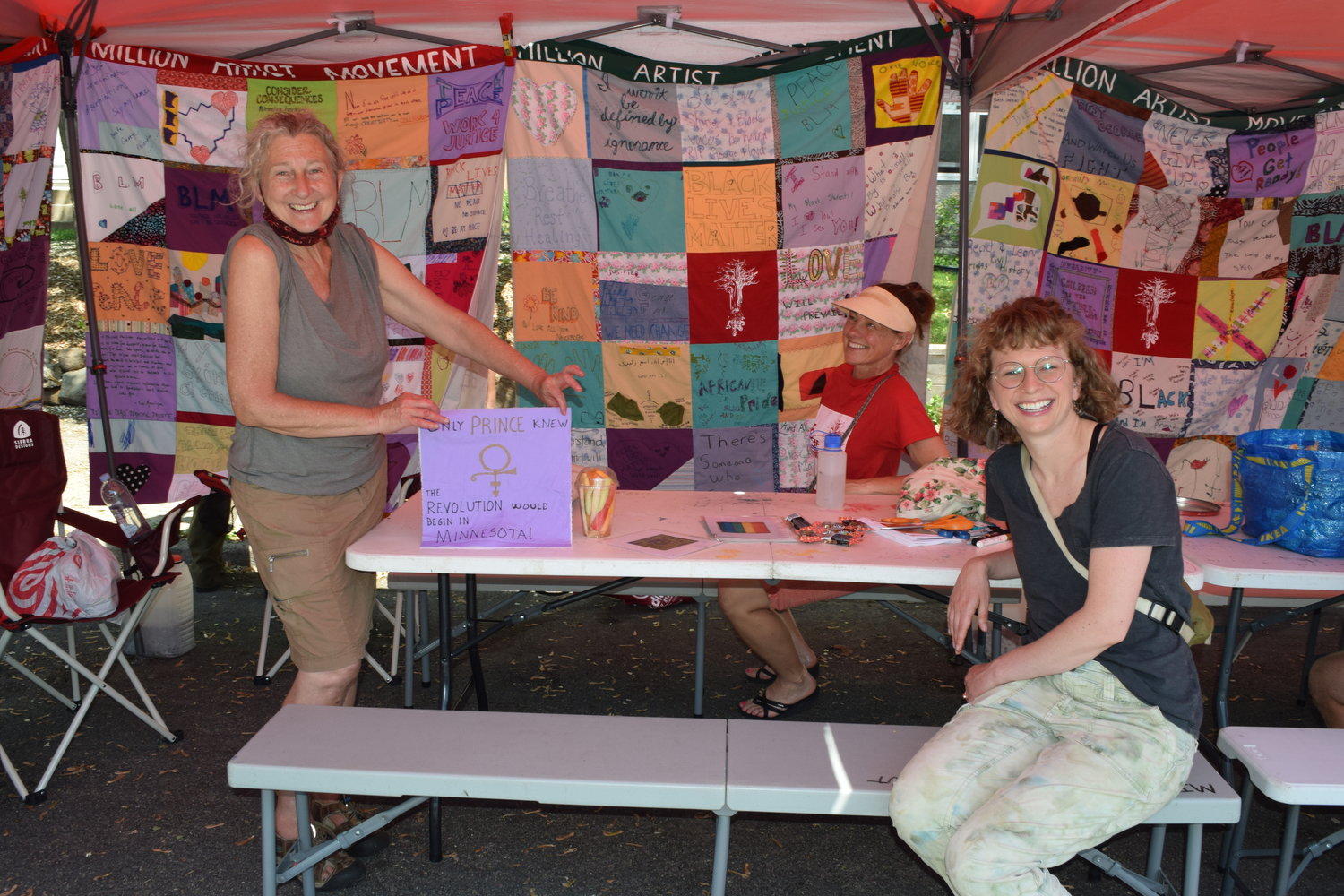Beneath a canopy draped with quilt squares that were created during the uprising in May 2020, Sandy Spieler, Kelley Skumautz and Julia Snider Nickerson (from left to right) offer materials for people to make a square of their own as part of the Million Artist Movement.