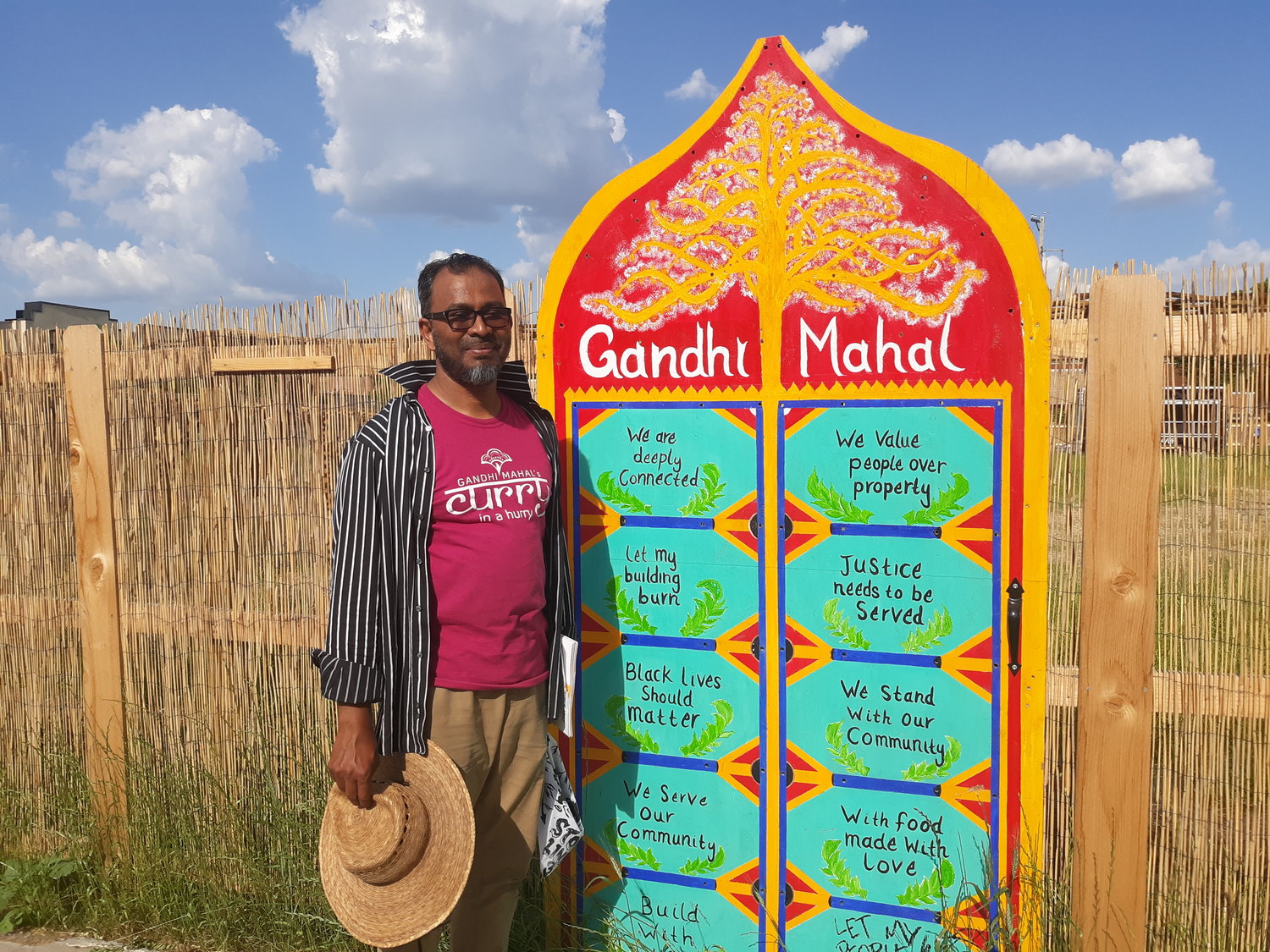 Gandhi Mahal owner Ruhel Islam stands by a gate at 3009 27th Ave. on which statements that drive them are written, including "We are deeply connected. We value people over property. Justice needs to be served. We stand with our community." He plans to rebuild at the site of the former building, but said it will take several years to make it happen. (Photo by  Jan Willms)
