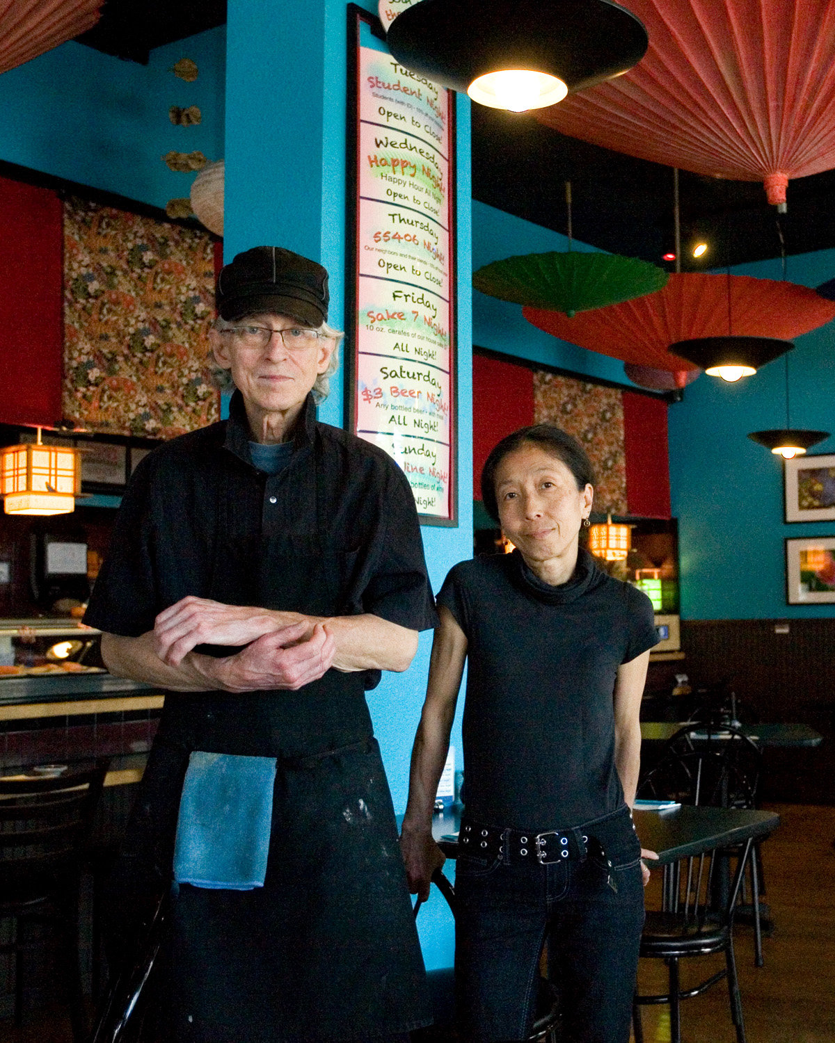 Midori Flomers (right), originally from Nagasaki, Japan, and John Flomers (left) originally from Brooklyn, N.Y., pictured in their former restaurant. They will be re-opening in a new Longfellow location as soon as they are able. In the meantime, find their take-out at the Seward Café Friday through Sunday evenings until further notice. (Photo by Margie O’Loughlin)