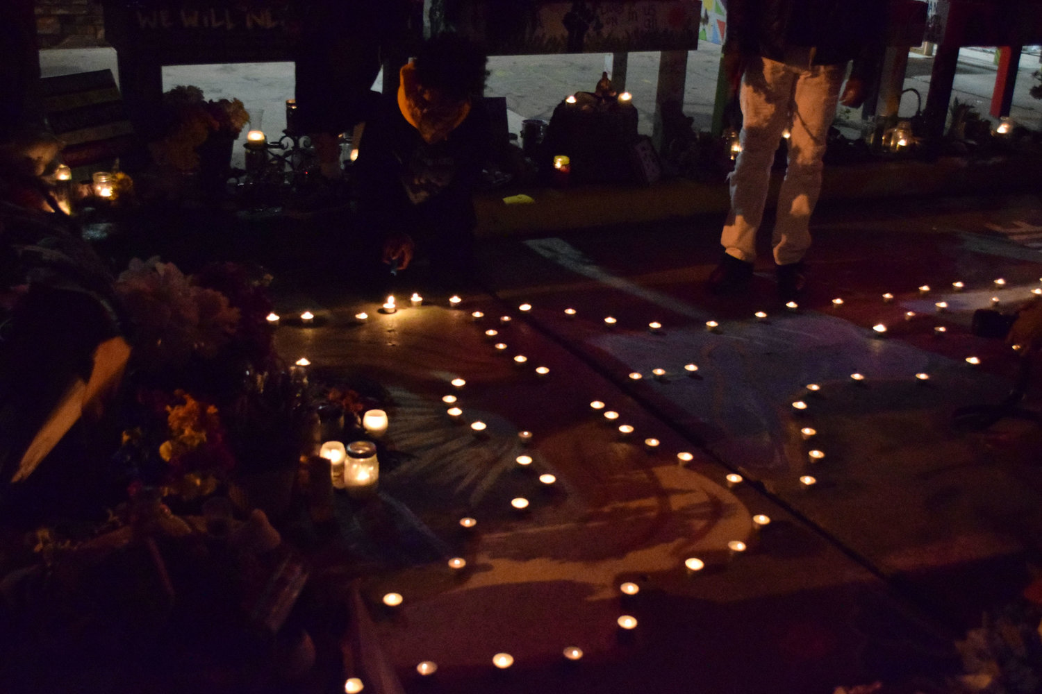 Community members place candles around the angel painted on the street in front of Cup Foods.