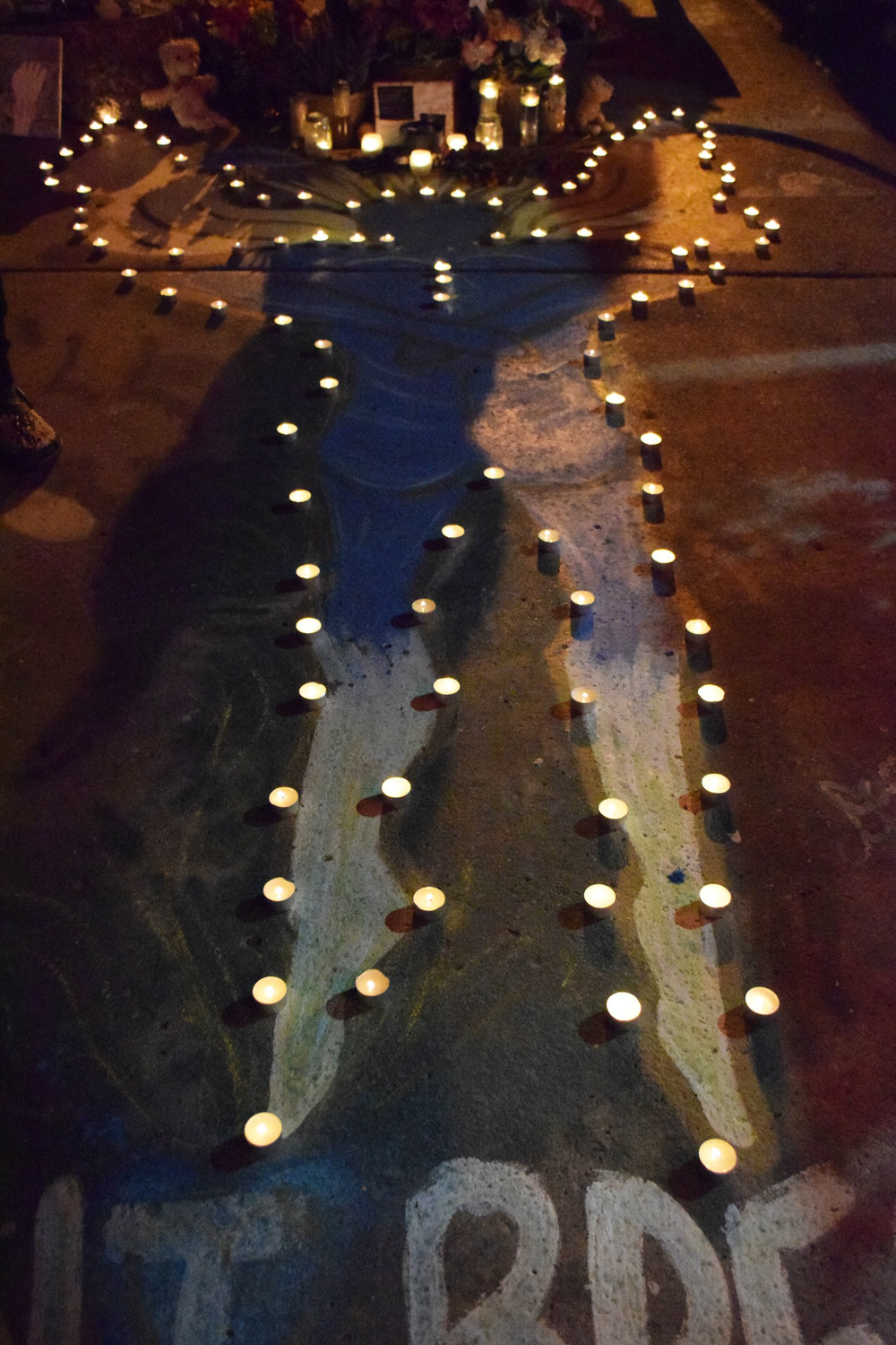 Community members place candles around the angel painted on the street in front of Cup Foods.