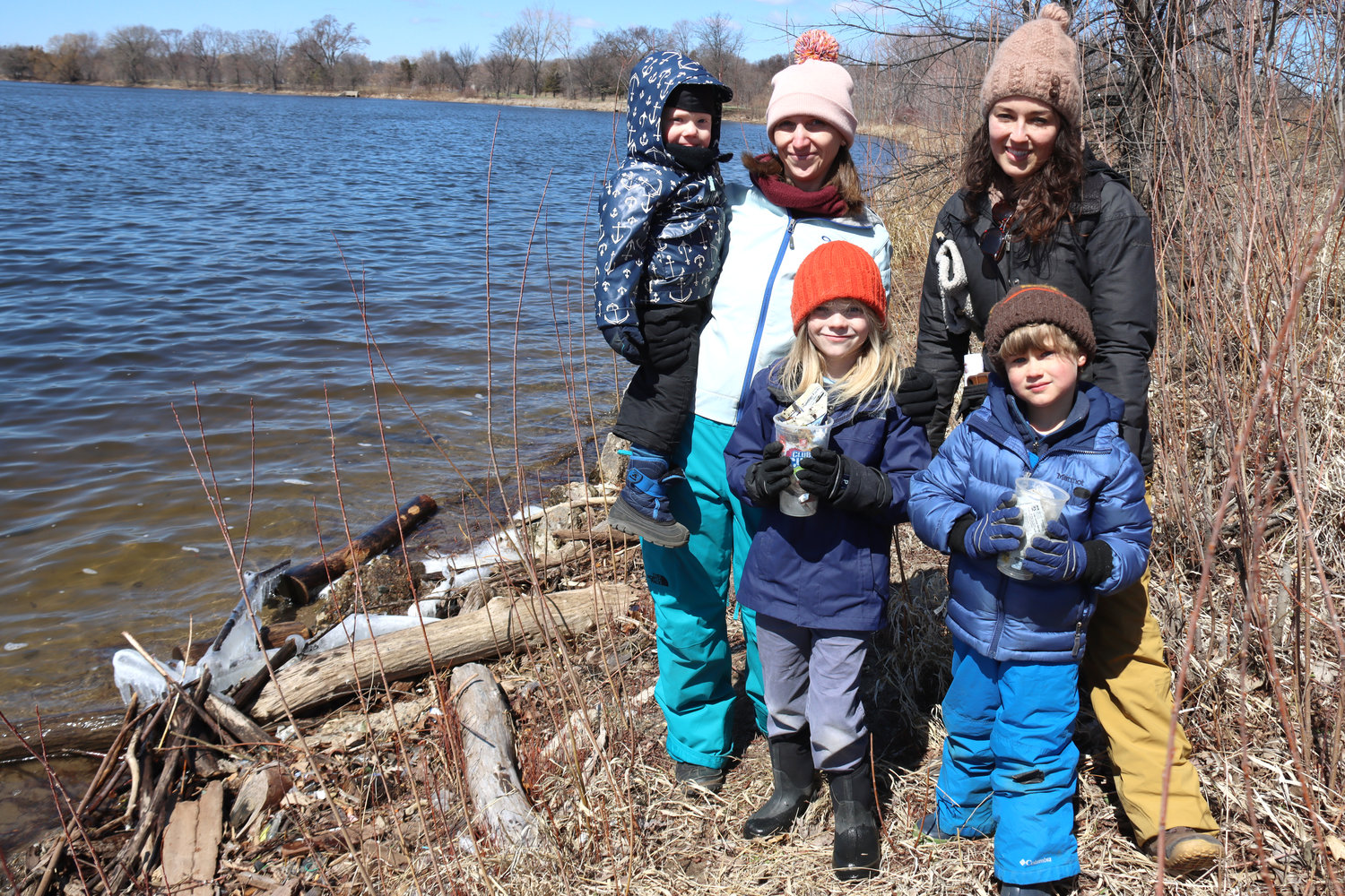 Nicole Cavender (left), who is Dakota, with Weston, 6, and Becket, 2.5 years, along with Ali Mailander (right) and Hap clean up trash along Lake Hiawatha on April 16, 2022. (Photo by Tesha M. Christensen)