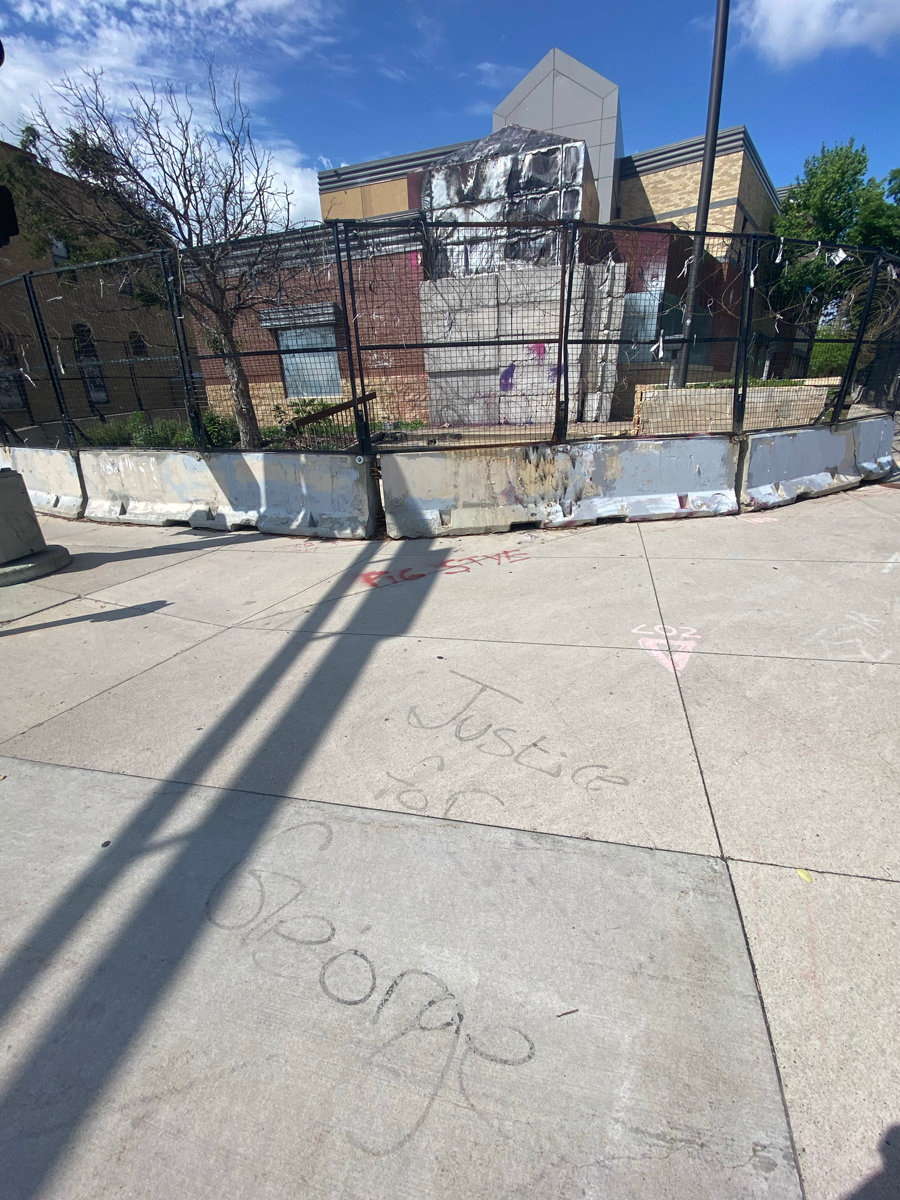 Justice for George is written on the sidewalk in front of the burnt 3rd Precinct which remains boarded and blocked with barb wire two years later. It still smells of burnt items as passersby walk down the sidewalk.