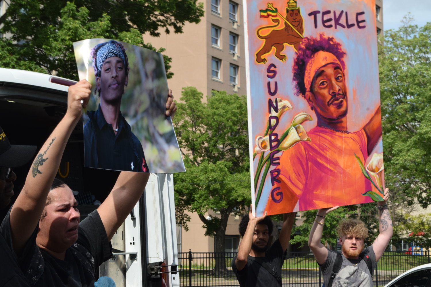 One of Tekle’s sisters holds up a picture of him as supporters raise a large portrait near the Seward apartment building where he was shot and killed by MPD. (Photo by Jill Boogren)