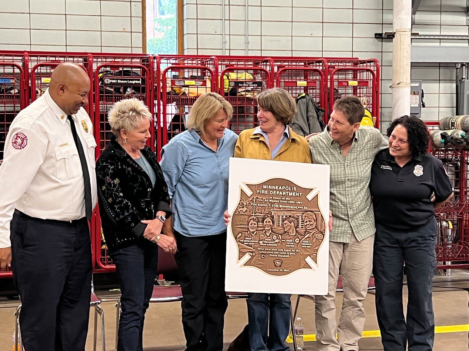 Minneapolis Fire Chief Bryan Tyner (at left) and Sherri Waisanen of the Women’s Firefighter Association (at right) present Vicki Hoff, Mary Mohn, Jean Kidd, Bonnie Bleskachek (center left to right) with a plaque honoring their place in history as the Minneapolis Fire Department’s first all-women crew.