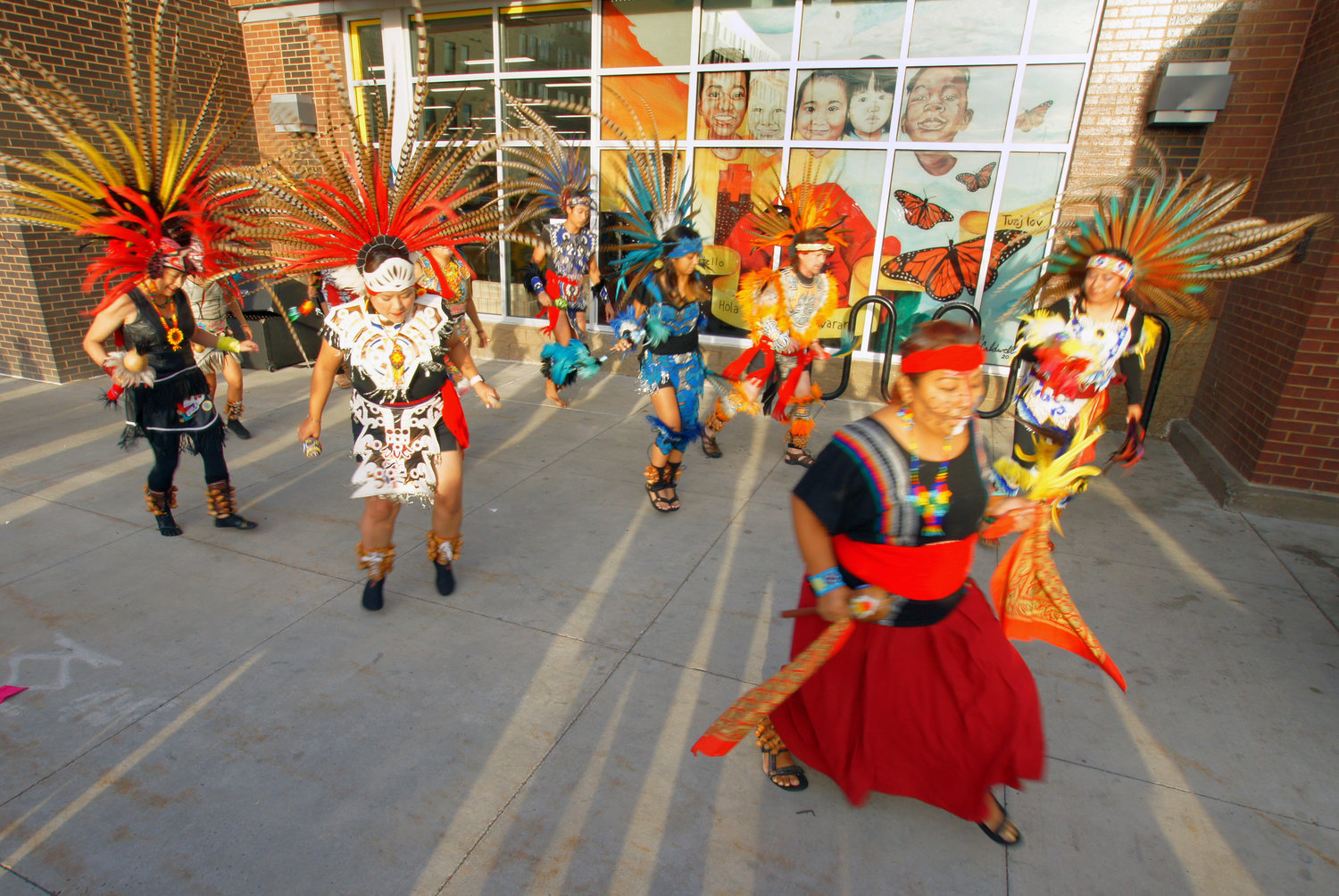 Kalpulli Ketzal Coatlicue Dance Troupe performs during a mural unveiling at Wells Fargo (2919 27th Ave. S.) on Sept. 22, 2022. Artist Charles Caldwell, a lifelong Minneapolis resident, set the mural against the city skyline. It celebrates the cultural diversity of south Minneapolis and includes symbols of peace (dove), hope (children), and transformation (butterfly). A yellow ribbon offers a greeting in six languages: Ojibwe, English, Spanish, Somali, Chinese, and Hmong. (Photo by Terry Faust)