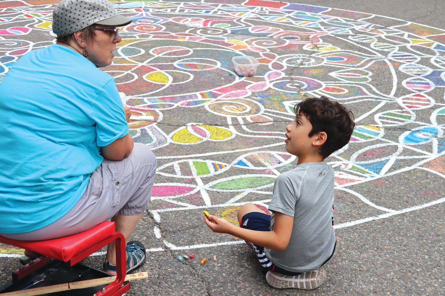 Chalk artist Sandy Forseth works on her street mandala with nine-year-old Archer Mandelman of northeast Minneapolis. Sponsoring this year’s event were the Southwest Connector, Linden Hills Dentistry, Larue’s, Heart of Tibet, Lakes Area Realty, the Harriet Brasserie, Heartfelt, and Linden Hills Neighborhood Council.