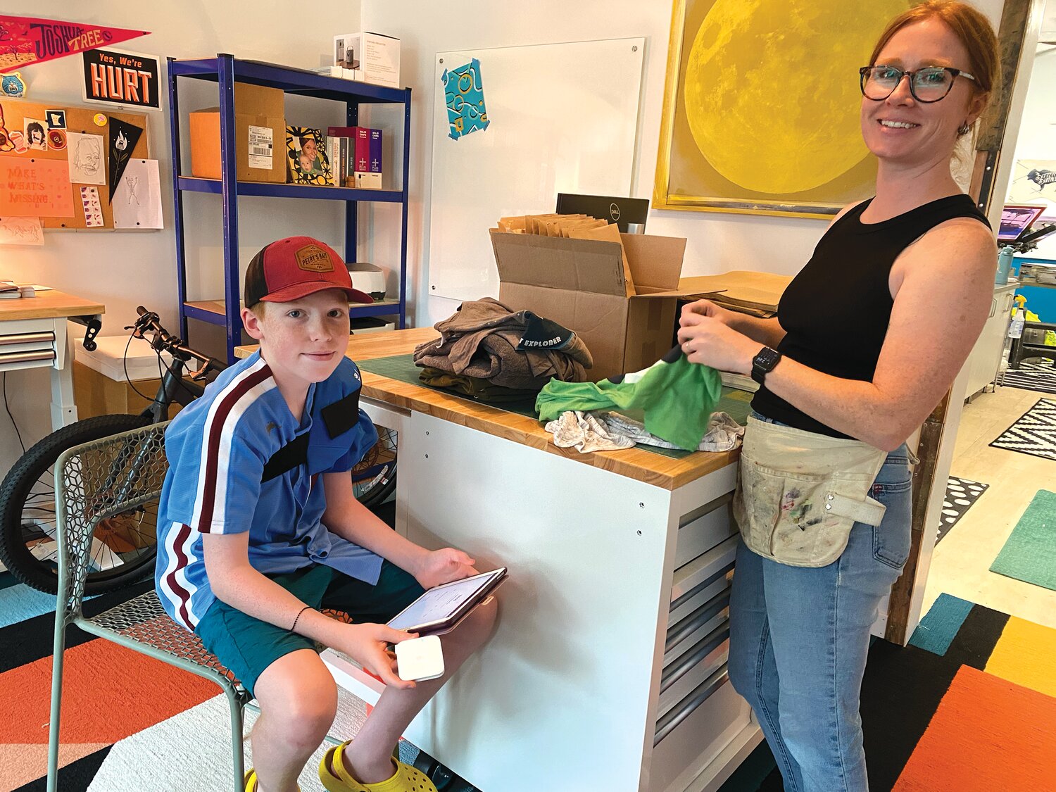 Ari Edgeton, age 12, assists his mom, Gillian McLaughlin, at Bitter Buffalo (4557 S 34th Ave.) on Aug. 6. People could do their own screen printing on t-shirts and flags during the event. McLaughlin's business moved from northeast Minneapolis into the Nokomis area about a year ago.