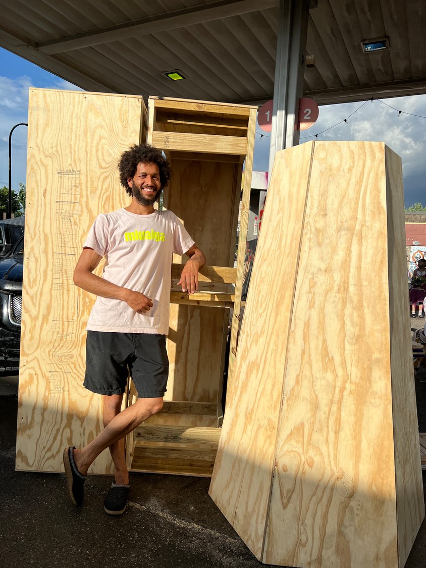 jordan powell karis stands in front of the wooden components of the new fist sculpture he is constructing for Akron, Ohio.