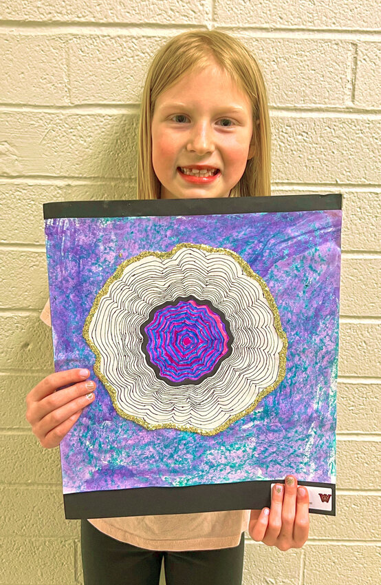 A third grader displays her 2D geode drawing featuring concentric shapes, contour lines, and a textured, pastel background.