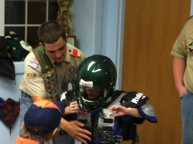 Jake Teixeira, captian of the DR Football Team and Eagle Scout,  assists a Tiger Scout trying on some football equipment