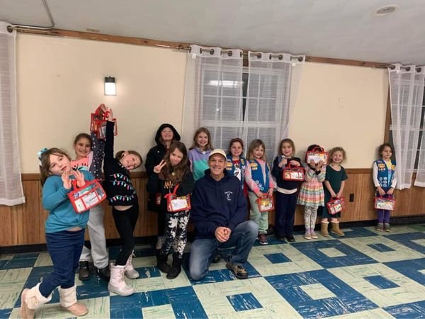 Members of Girl Scout Daisy/Brownie Troop 989 are shown holding the first aid kits they made.  The kits were given to Mr. Carl Sweeney (center) of Hope and Faith Drive for distribution.