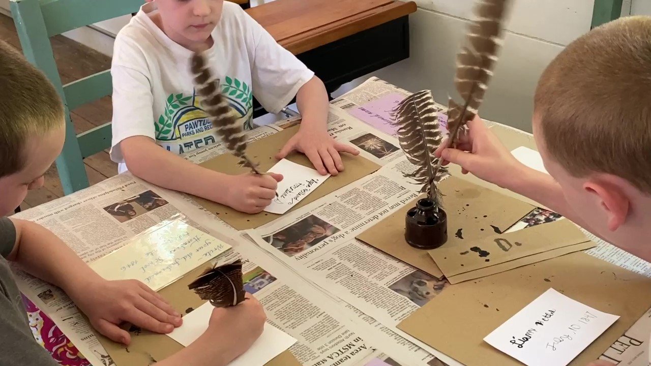 Three young visitors writing with our feather pens.