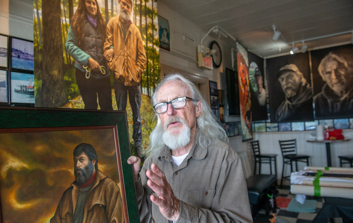 Sitka artist Steve Lawrie holds up a decades-old painting he did of fisherman Grant Miller, in front of more recent works. The paintings, part of Lawrie's exhibit 