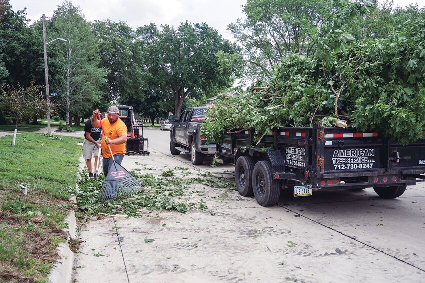 Workers with American Tree Service of Holstein rake up debris along West Cedar Street Tuesday afternoon. 