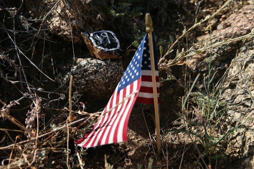 An American flag and a stone with “19” painted on it rest next to one of the plaques on the trail in the Granite Mountain Hotshots Memorial State Park in Yarnell. A plaque for each of the fallen members of the Granite Mountain Hotshots is placed along the trail to the memorial site. (Photo by Joey Plishka/Cronkite News)