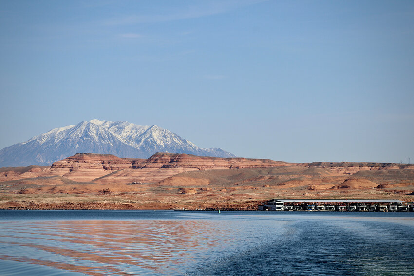Snowy mountains loom behind lake Powell near Hall's Crossing on April 10, 2023. The nation's second-largest reservoir expects a big boost from snowmelt this year, but scientists say one wet winter will not be enough to turn around the Colorado River's supply-demand crisis. (Photo by Alex Hager/KUNC)