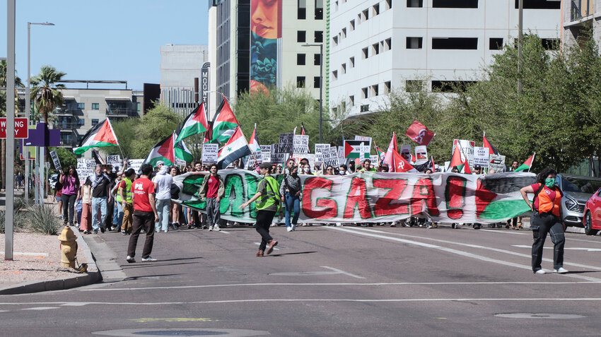 A protestor named Firas, left, in a red PSL shirt, leads a March 30 march, along with security members, down North Third Street in Downtown Phoenix. Chanting:“Stop the violence,” Firas is an American-Afghani member of PSL who grew disillusioned with American foreign policy after the U.S. invasion of Afghanistan in the early 2000s. 
