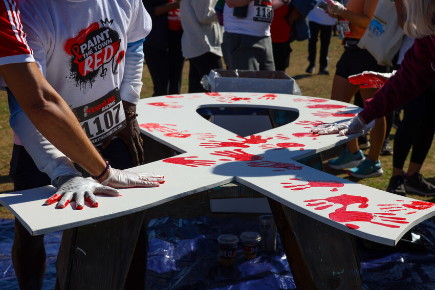 Event attendees make paint handprints to turn a white wooden “ribbon” red – signifying blood cancers – at the Aunt Rita’s Paint the Town Red AIDS Walk Arizona & 5K Run on Saturday, April 6, at Tempe Beach Park. (Photo by Kayla Mae Jackson/Cronkite News)