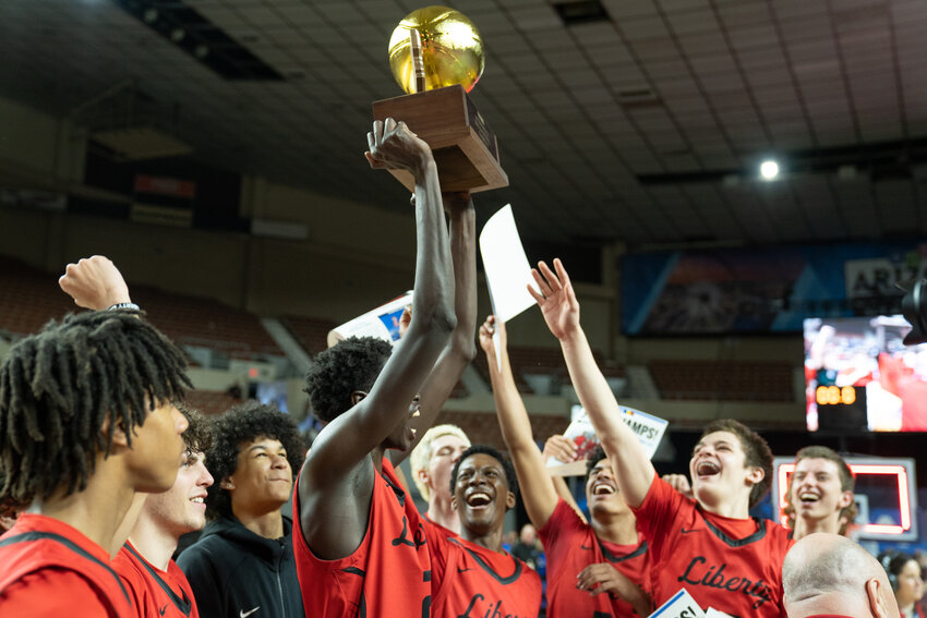 Ring Nyeri raises the 6A boys basketball trophy high as his teammates celebrate.the school's first state basketball title.