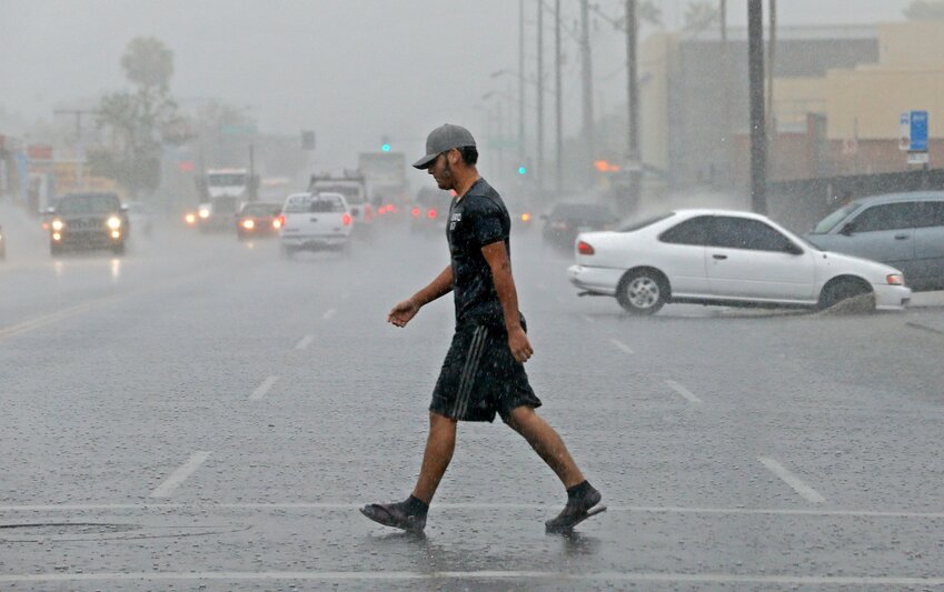 A pedestrian walks across a rain-drenched streets as storms push through the Phoenix metro area.