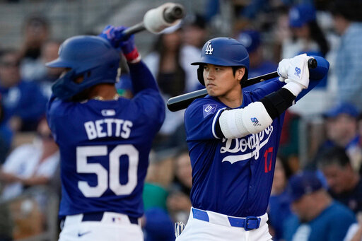 Los Angeles Dodgers' Mookie Betts (50) and Shohei Ohtani warm up on deck before a spring training baseball game against the Cincinnati Reds on Friday, March 8, 2024, in Phoenix. The game was canceled because of rain. (AP Photo/Carolyn Kaster)