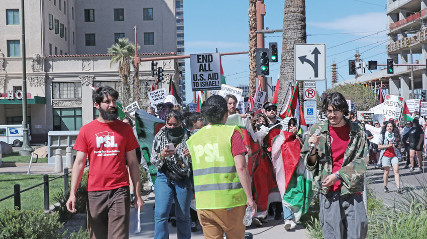 Firas, a security person and a speaker march down North Central Avenue into Civic Space Park on March 30. The poster behind them reads&ldquo;End all U.S aid to Israel.&rdquo;