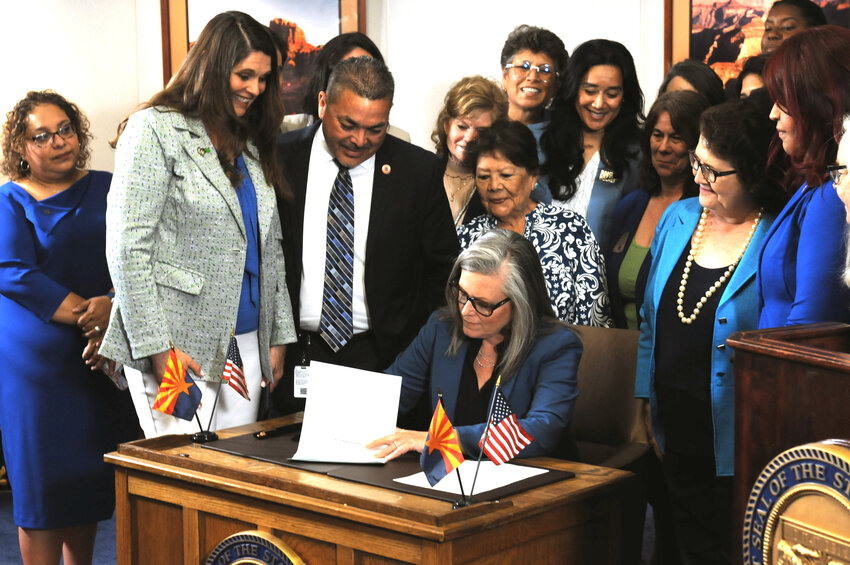 Gov. Katie Hobbs signs legislation Thursday to repeal the 1864 law that outlaws most abortions, though it cannot take effect for more than three months. Looking over her right shoulder are Rep. Stephanie Stahl Hamilton, who sponsored the bill, and House Minority Leader Lupe Contreras. (Capitol Media Services photo by Howard Fischer)