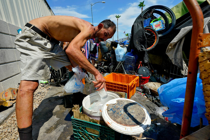 Kevin Hendershot pours ice into a bucket outside his tent in &ldquo;The Zone,&rdquo; homeless encampment, July 14, 2023, in downtown Phoenix. (The Associated Press/Matt York)
