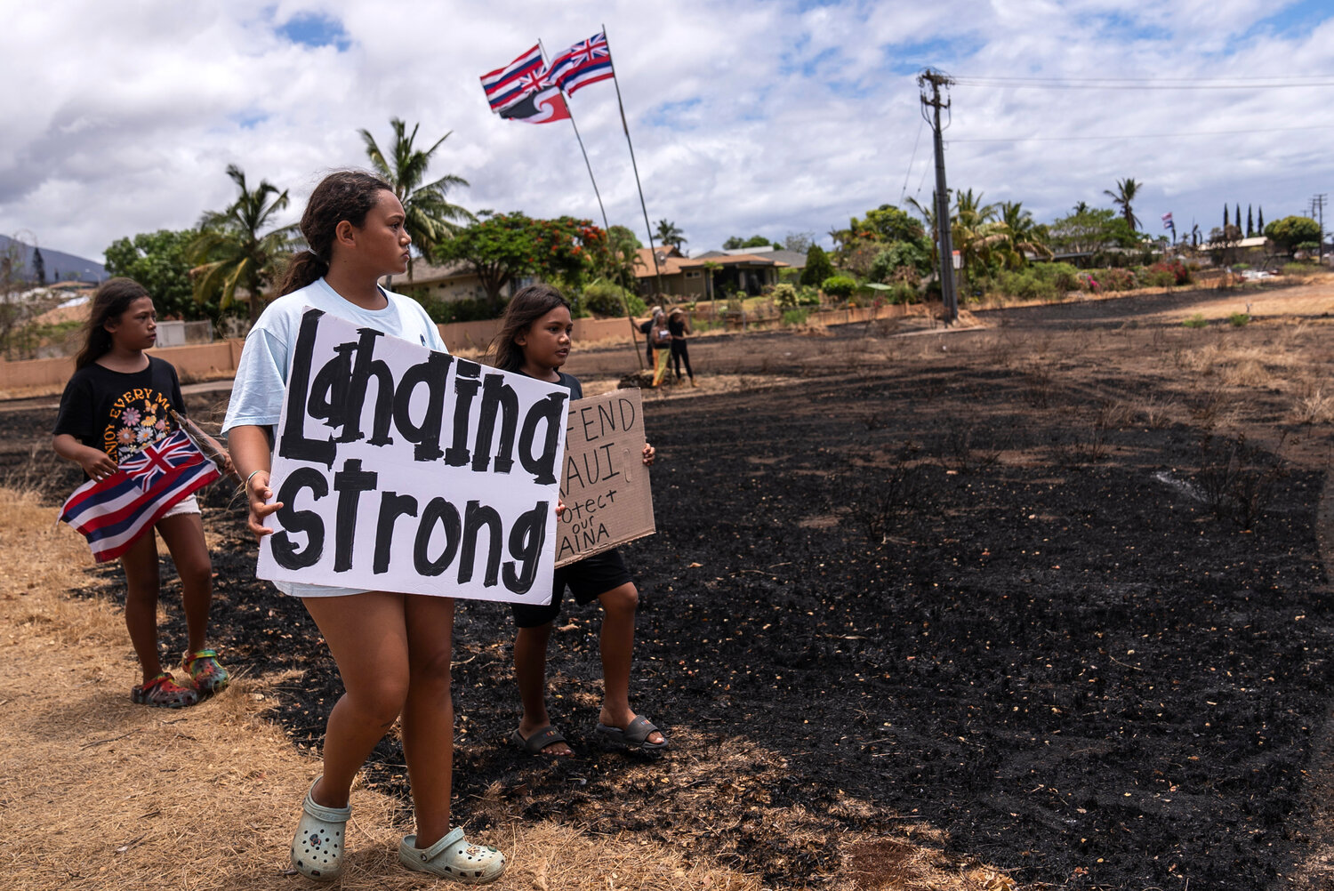 Children hold signs and a Hawaiian flag in Lahaina, Hawaii, on Aug. 21, 2023.