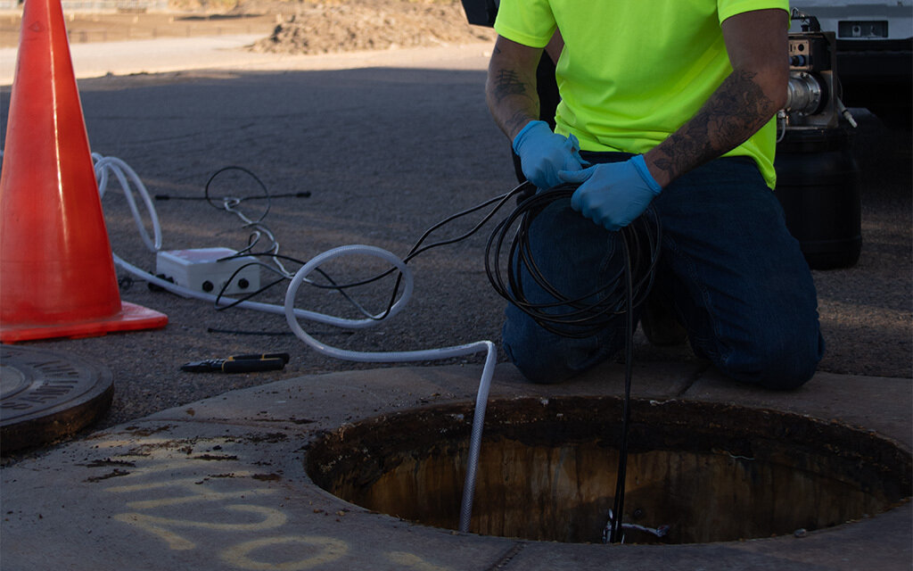 An employee of RDH Environmental Services installs a Kando Pulse device inside a sewer system near Broadway Road and 83rd Avenue in Phoenix on Nov. 8, 2023. (Photo by Ellie Willard/Cronkite News)