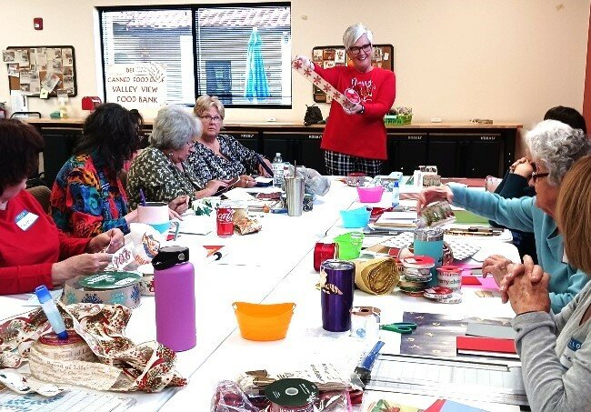Instructor Lloydyne Vining at the head of the table holding a sample of glittering Christmas ribbon to be cut apart and incorporated into a greeting card.