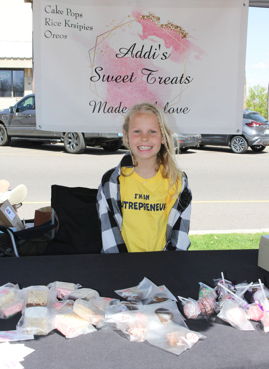 Entrepreneur Addison Barclay sells homemade cake pops, Rice Krispie treats, and Oreos at an outdoor market.